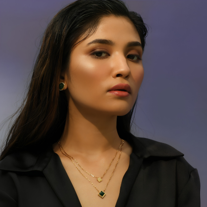 legant woman wearing layered gold necklaces with a delicate green gemstone pendant and matching earrings.