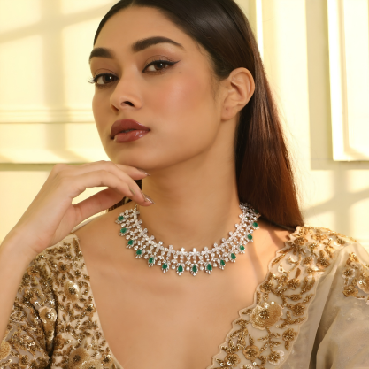 A woman wearing a statement silver necklace with green gemstones, styled with an embellished traditional outfit.