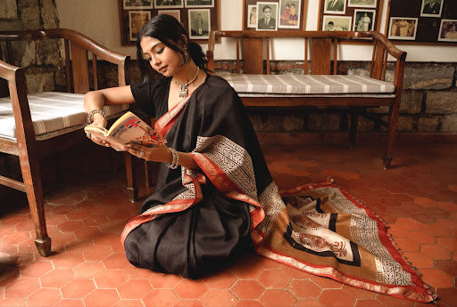 Woman in a black saree wearing traditional jewelry indoors.